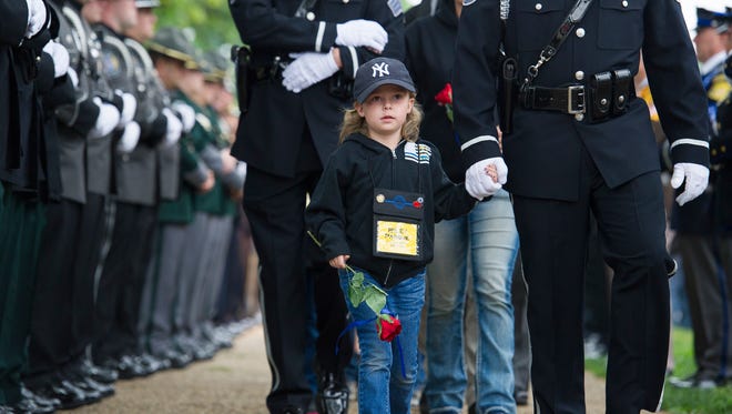 Riley Parque, 5, holds the hand of a police officer as her family arrives for the National Law Enforcement Officers Memorial Fund 30th annual Candlelight Vigil. Riley's father, police officer Chad Parque, of the North Las Vegas Police Department, died in the line of duty Jan. 1, 2017.
